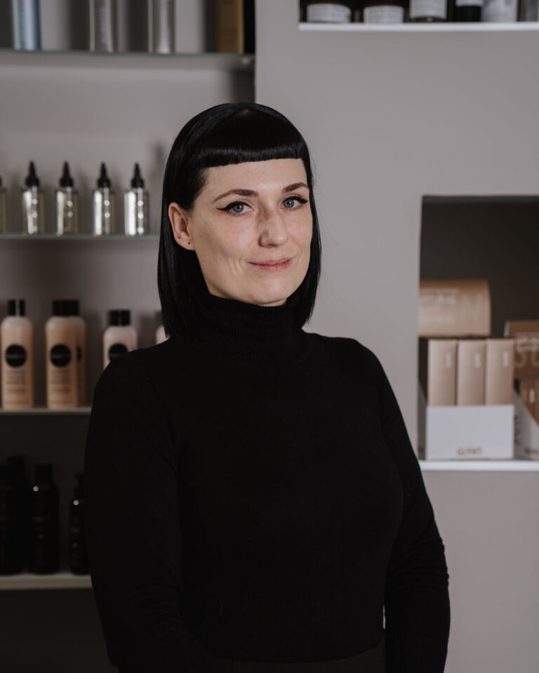 Friseurin Mandy steht im Salon Helena Conzen Hairdesign in Bochum vor einem Regal mit Haarpflegeprodukten.