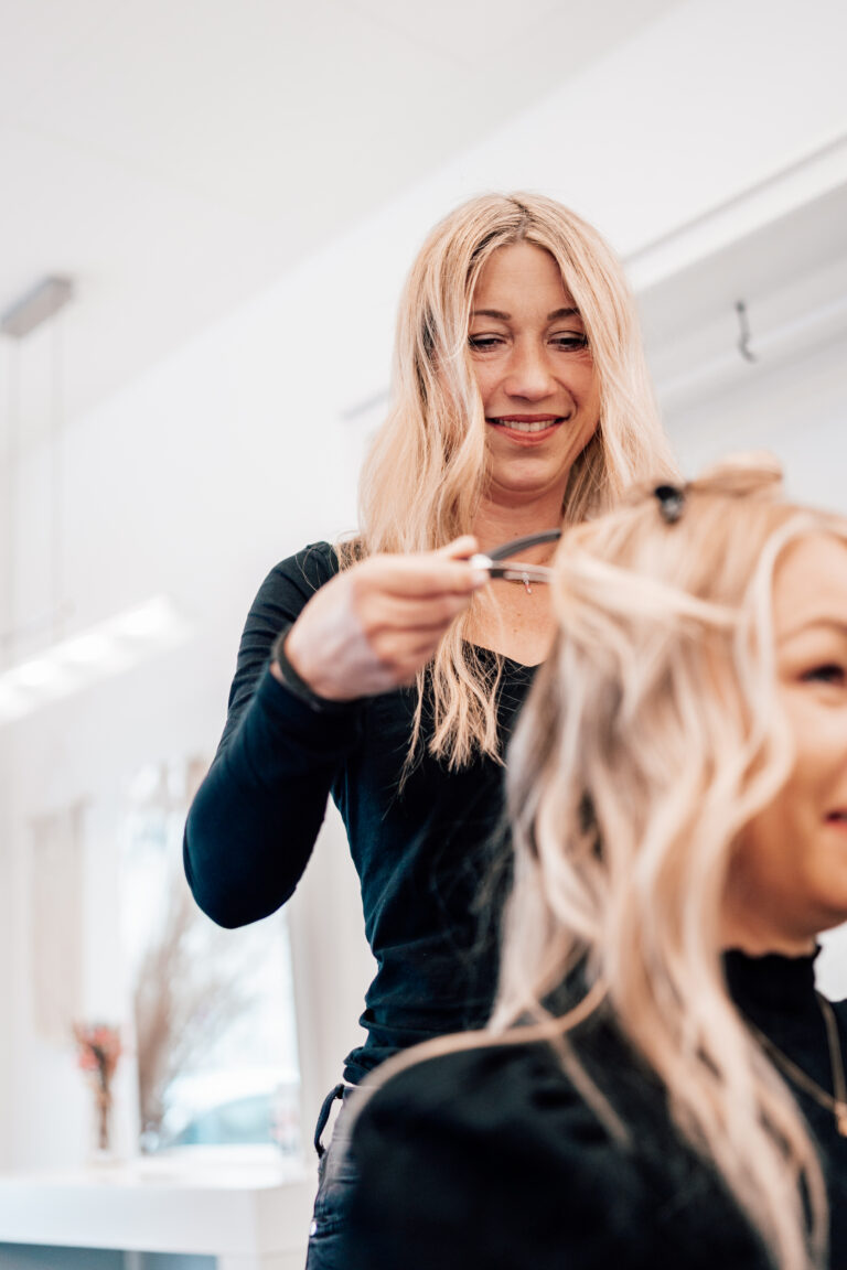 Friseurin trägt Balayage-Farbe auf blonde Haare einer Kundin auf