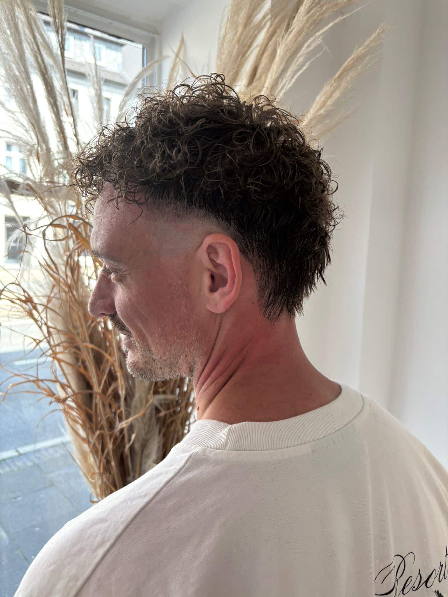 Mann mit lockigem Mullet und kurzem Fade-Schnitt im Profil